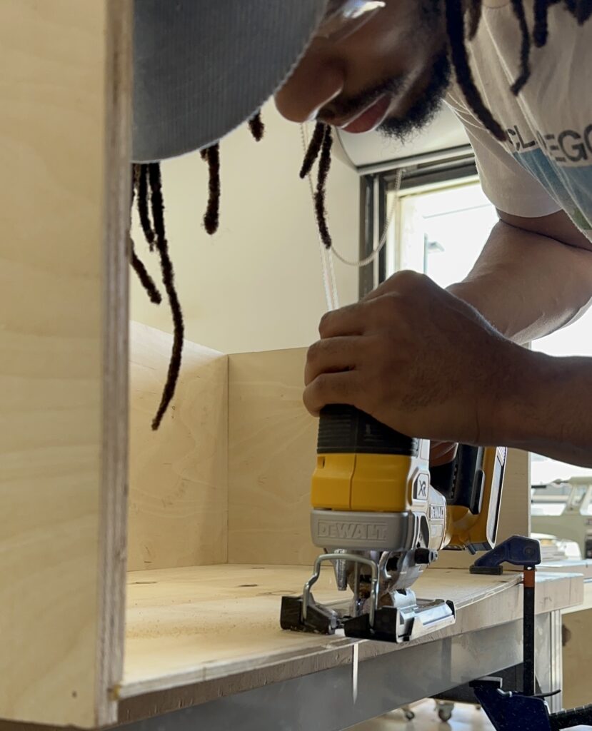 A person uses a jig saw to cut plywood in a shop environment